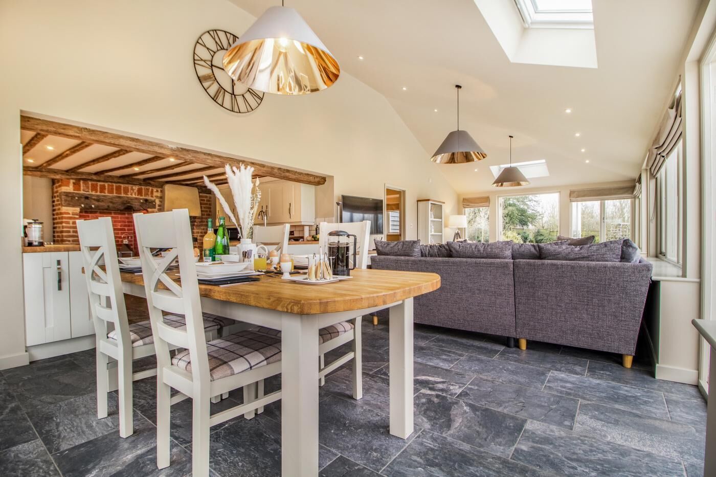 A modern kitchen with a dining area, a sofa, and a large window.
