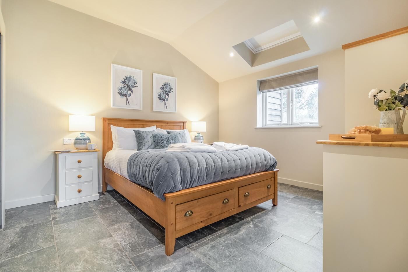Una camera da letto con un letto di legno, comodini, una finestra e opere d'arte appese al muro.