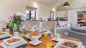 Une table en bois dressée pour le petit-déjeuner, avec des assiettes de céréales, des croissants et du jus d’orange.