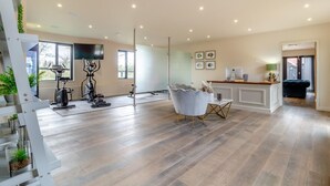 Un vaste espace de vie comprenant une cuisine moderne, du matériel de fitness et un coin salon avec une table basse en verre.