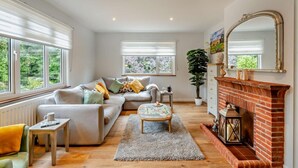 Una sala de estar con sofá, mesa de centro, chimenea y ventanas amplias.