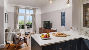 A modern kitchen with a large island, a dining area with a sofa, and a TV in the background. - 5 Bed in Seahouses (oc-s29053) (Seahouses)