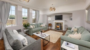 A spacious living room with a fireplace, two sofas, a coffee table, and a large window. - 5 Bed in Seahouses (oc-s29053) (Seahouses)