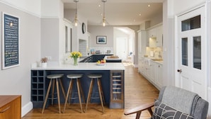 A modern kitchen with a central island, bar stools, pendant lighting, and a view into the dining area. - 5 Bed in Seahouses (oc-s29053) (Seahouses)