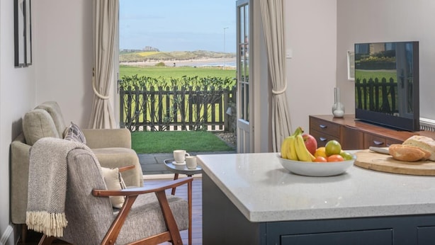 A living room with a large window, a sofa, a coffee table, a TV, and a fruit bowl. - 5 Bed in Seahouses (oc-s29053) (Seahouses)