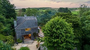 A house with a dark roof, a visible chimney, and a front door leading to a covered outdoor area with seating. - 5 Bed in Little Petherick (oc-s29057) (Little Petherick)