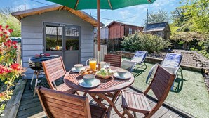 Una terraza de madera con una mesa redonda, sillas y un paraguas verde.