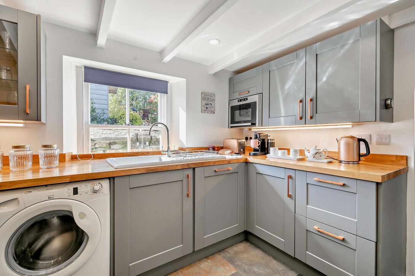 A modern kitchen with grey cabinets, a washing machine, a microwave, and a coffee maker.