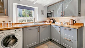 Una cocina moderna con gabinetes grises, lavadora, microondas y cafetera.