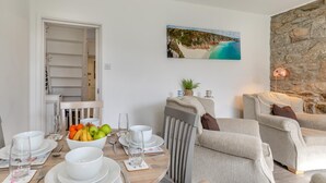 A dining area with a table set for four, a stone wall, and a painting of a coastal scene. - 2 Bed in Mousehole (oc-d29111) (Mousehole)