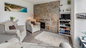 A living room with a stone wall, two armchairs, a fireplace, a TV, and a bookshelf. - 2 Bed in Mousehole (oc-d29111) (Mousehole)