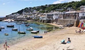 A coastal town with boats docked along the shore, a sandy beach, and houses built on a hillside. - 2 Bed in Mousehole (oc-d29111) (Mousehole)