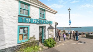 A building named 'The Mousehole' with a signboard, a small shop window, and a view of the sea. - 2 Bed in Mousehole (oc-d29111) (Mousehole)