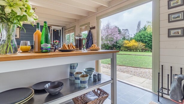 Una cucina moderna con un piano di lavoro in legno, diversi utensili da cucina e vista su un giardino attraverso una porta aperta.