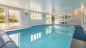 Una grande piscina coperta con pareti in vetro trasparente, un orologio a parete e una panca lungo il bordo.