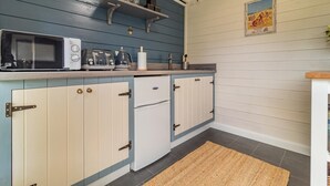 Una cucina con una combinazione di colori blu e bianco, con forno a microonde, tostapane e bollitore sul piano di lavoro, e un piccolo ripiano sopra.