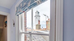 Een kamer met een raam, uitzicht op een vuurtoren en een bakstenen gebouw.