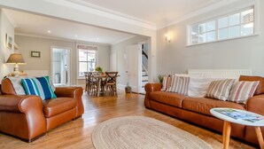 Een ruime woonkamer met een bruine leren bank, een ronde salontafel en een eethoek met een houten tafel en stoelen.