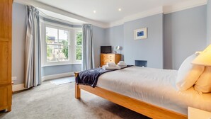 Een slaapkamer met een houten bed, een nachtkastje, een televisie en een raam met gordijnen.