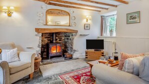 Una sala de estar acogedora con chimenea de piedra, vigas de madera, televisor y asientos cómodos.