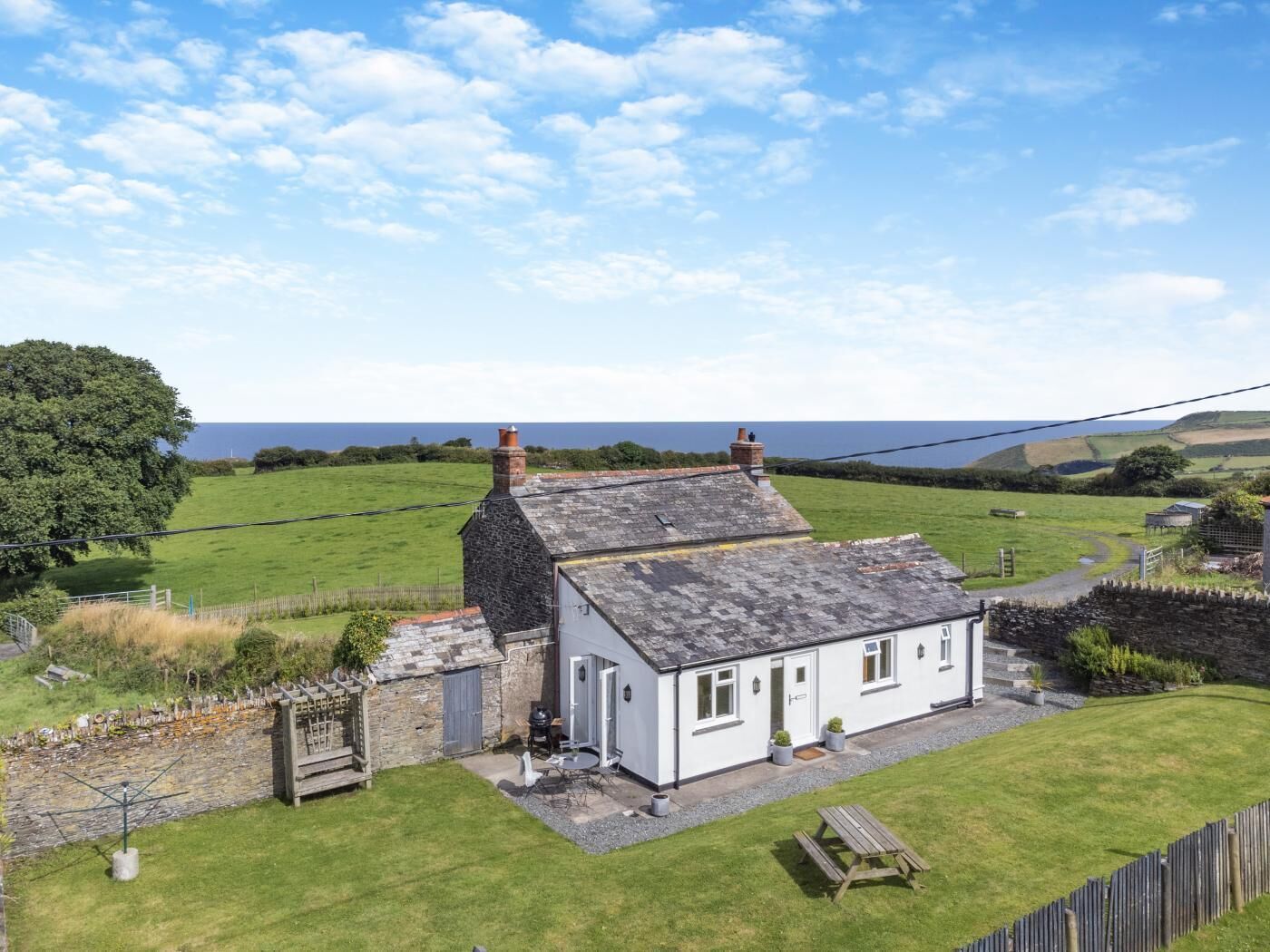 A white cottage with a stone chimney, a small garden, and a view of the sea.