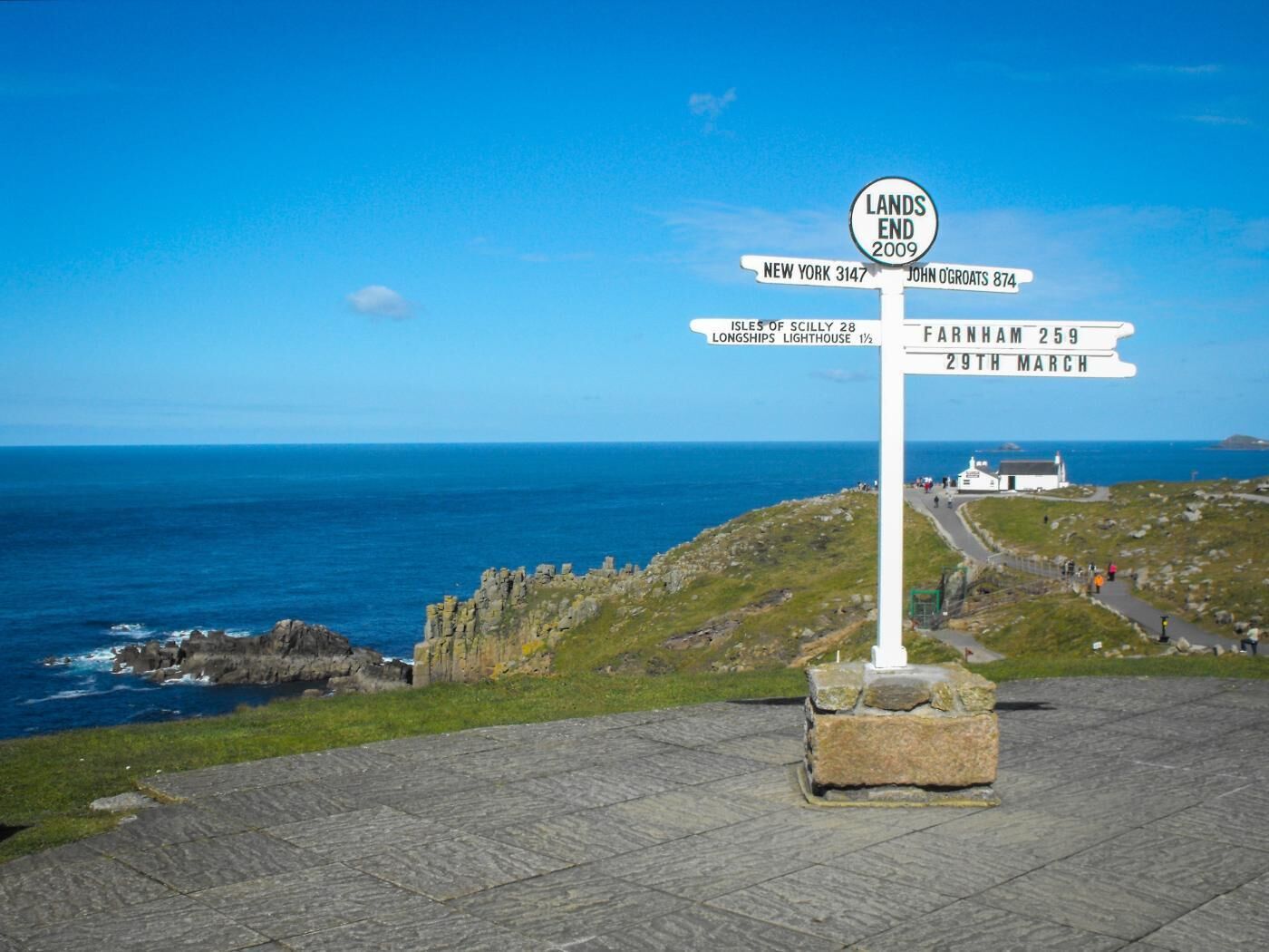 A signpost with directions to various locations including New York, John Ogroats, Isles of Scilly, Longships Lighthouse, and Farnham.