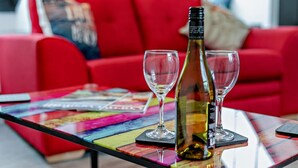 Un divano rosso, un tavolino in vetro con una bottiglia di vino e due bicchieri, e riviste colorate.