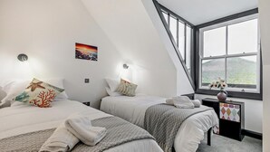 Una camera da letto con due letti, una finestra vista, un piccolo tavolo con un vaso e un quadro appeso al muro.