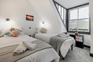 Un dormitorio con dos camas, una ventana con vistas, una mesita con un florero y un cuadro en la pared.