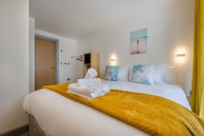 A hotel room with a bed, a wooden wardrobe, a wall-mounted shelf, and a painting. - 2 Bed in St. Ives (oc-e28156) (St Ives)
