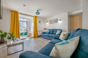 A living room with a sofa, a coffee table, yellow curtains, and a view through a window. - 2 Bed in St. Ives (oc-e28156) (St Ives)