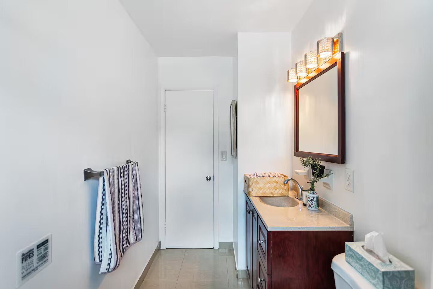 A modern bathroom with a white door, a vanity with a mirror and lights, and a towel rack with patterned towels.