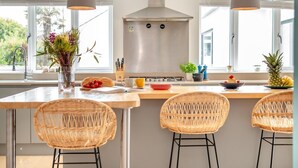 A modern kitchen with a central island, stainless steel appliances, and wicker chairs. - 4 Bed in St. Merryn (oc-t29153) (Saint Merryn)
