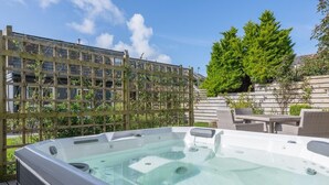 Ein Whirlpool auf einer Holzterrasse mit Holzzaun und Grünpflanzen im Hintergrund.