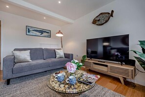Ein modernes Wohnzimmer mit einem grauen Sofa, einem Flachbildfernseher, einem Couchtisch mit Dekoration und einer Wanddekoration – einem montierten Fischskelett.