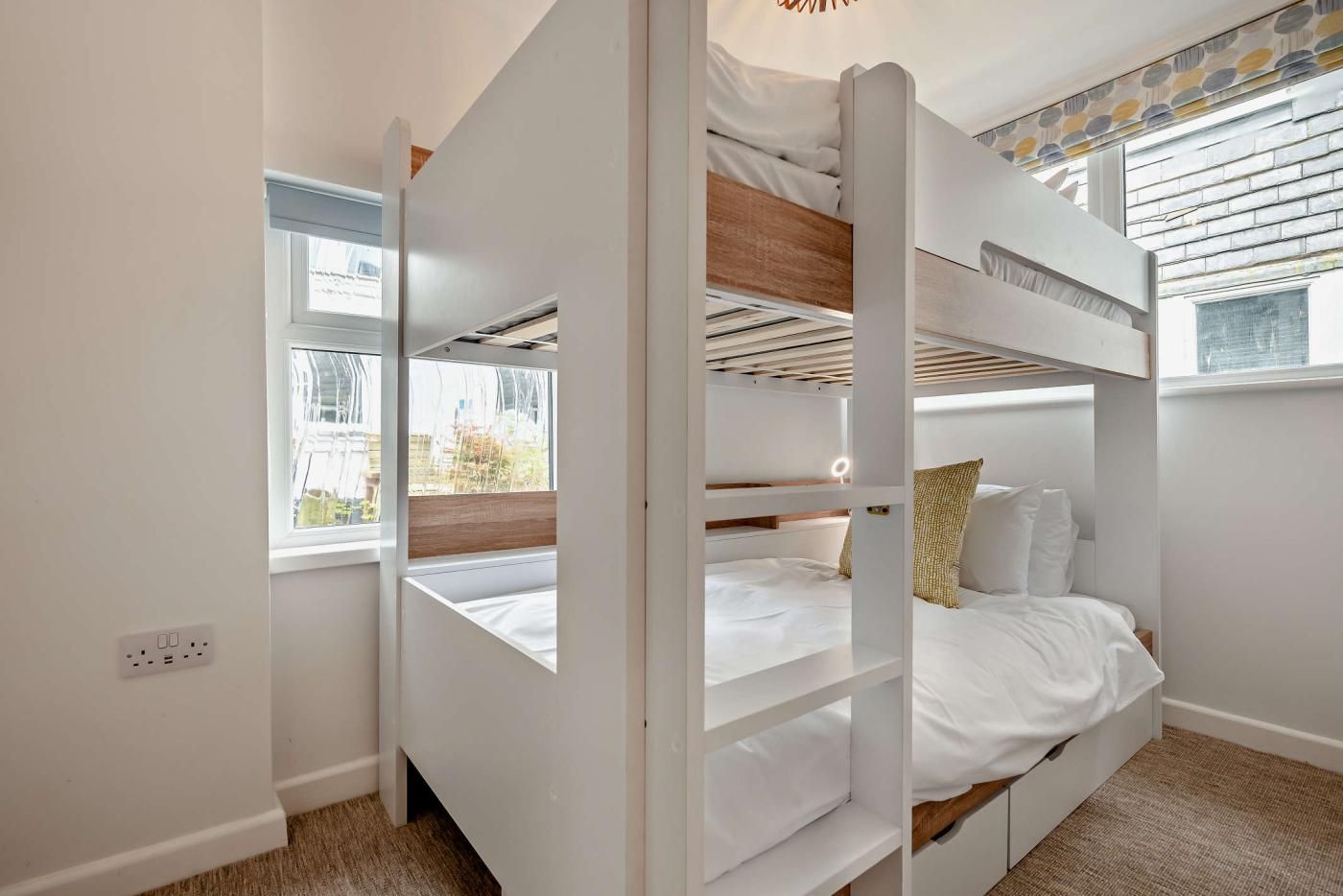 A bunk bed room with a window, a power outlet, and a patterned curtain.