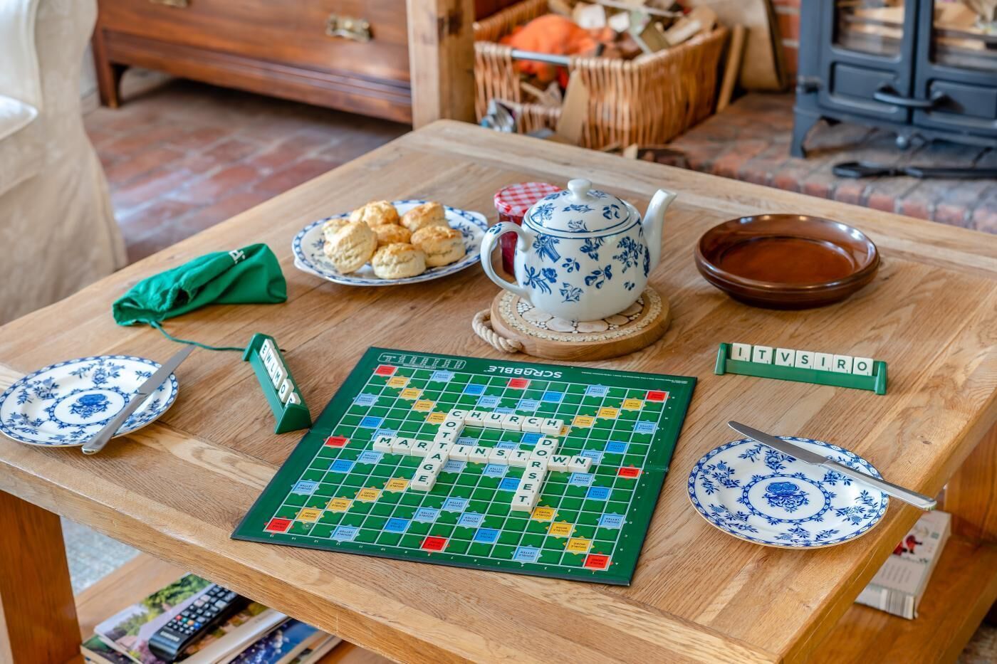 Un jeu de Scrabble est installé sur une table en bois, avec un plateau de jeu vert, une théière et une assiette de biscuits.