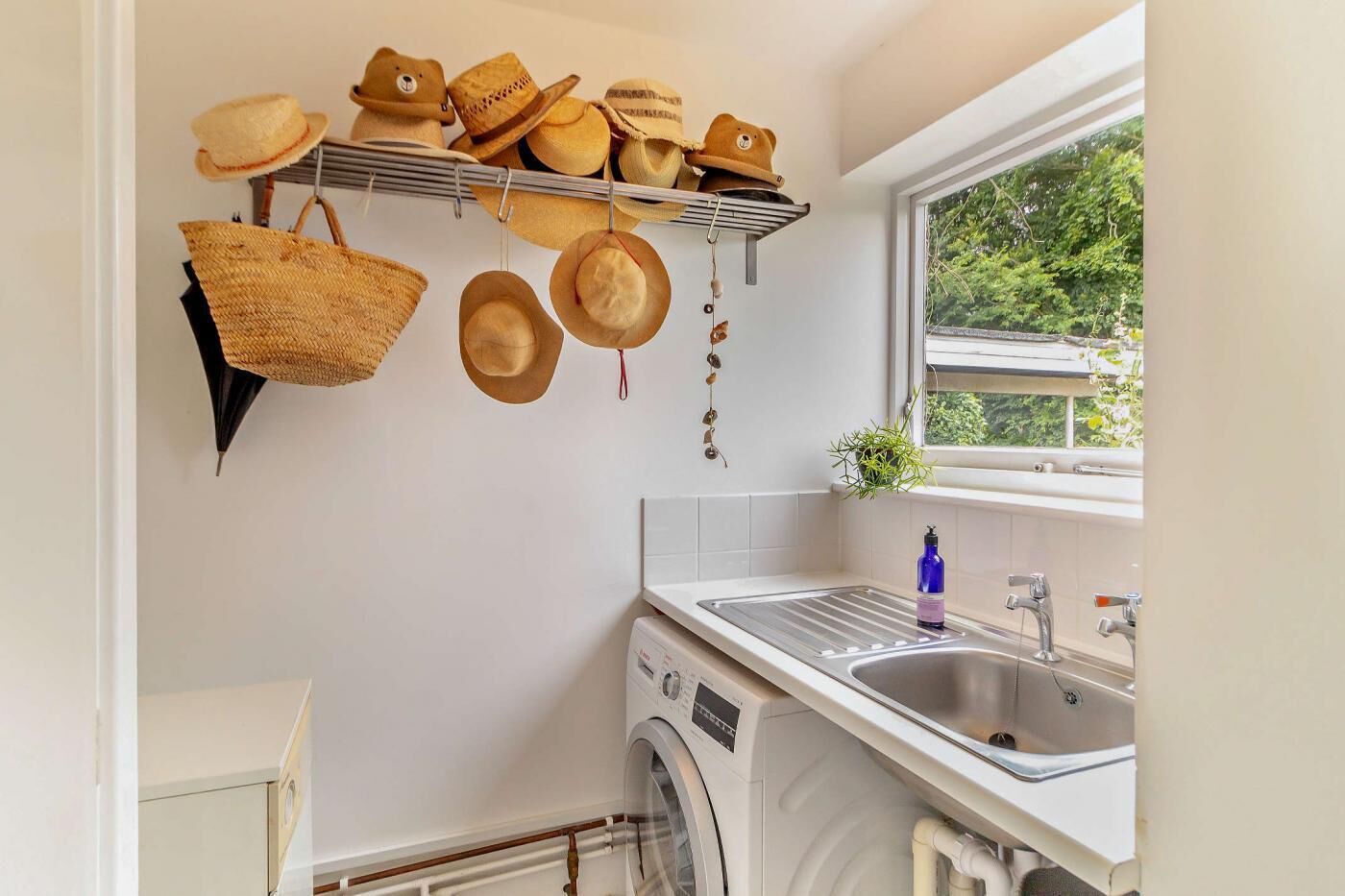 A kitchen with a washing machine, a sink, and a window with a view of greenery.
