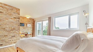 A bedroom with a brick wall, a large bed, a desk, and a window. - 3 Bed in Walberswick (oc-s29097) (Walberswick)