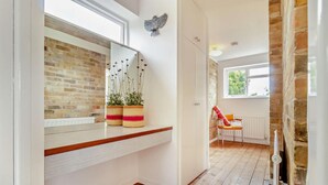 A hallway with a brick wall, a white door, a window, and a chair with a cushion. - 3 Bed in Walberswick (oc-s29097) (Walberswick)