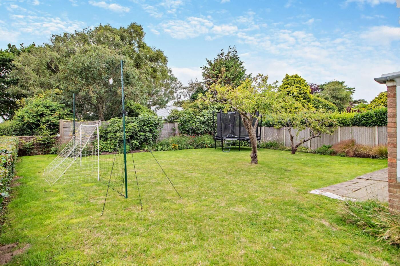 Un jardin avec un but de football, un trampoline et une clôture en bois.
