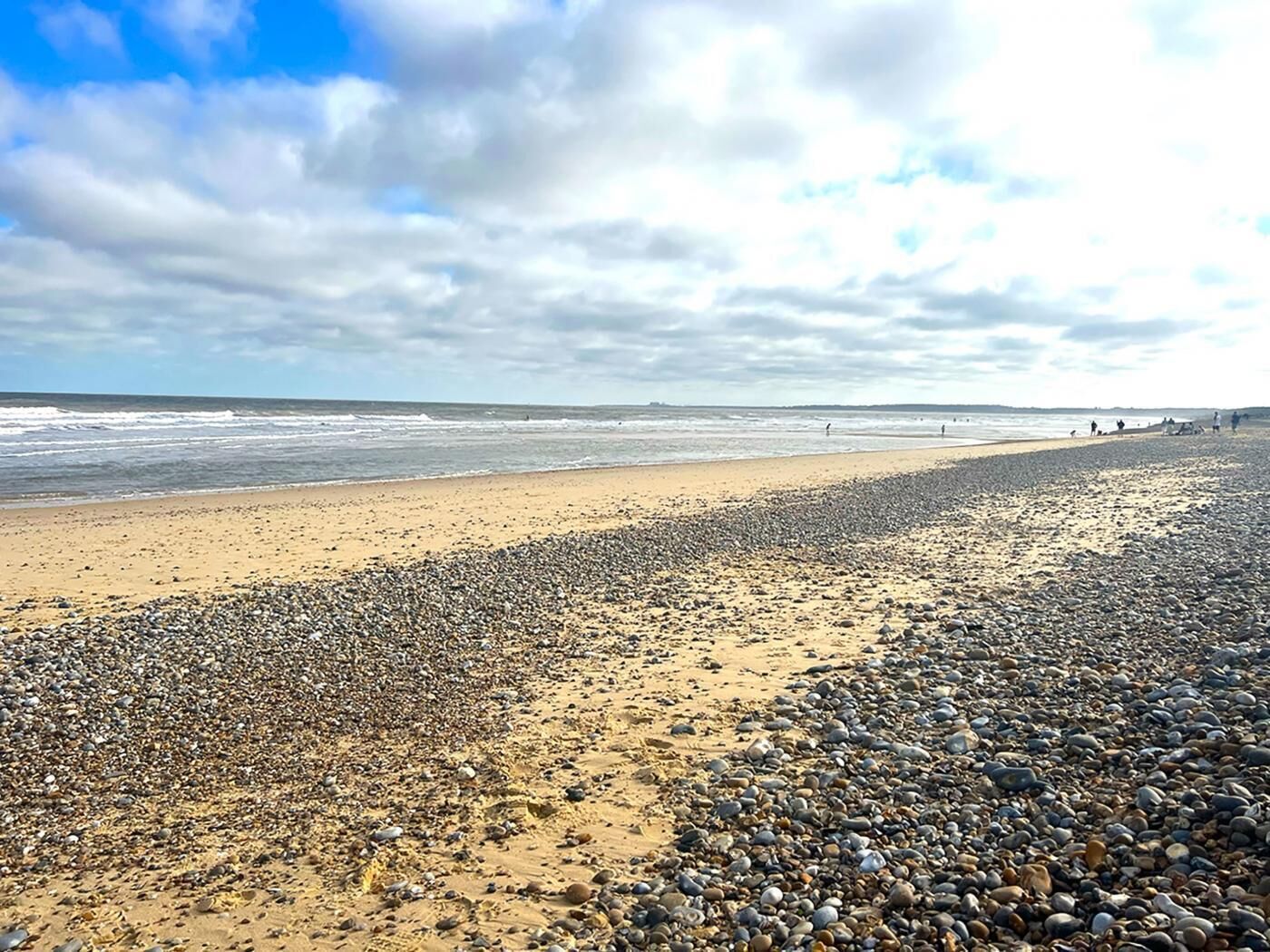 A pebbled beach with a wide sandy area and a calm sea under a partly cloudy sky.