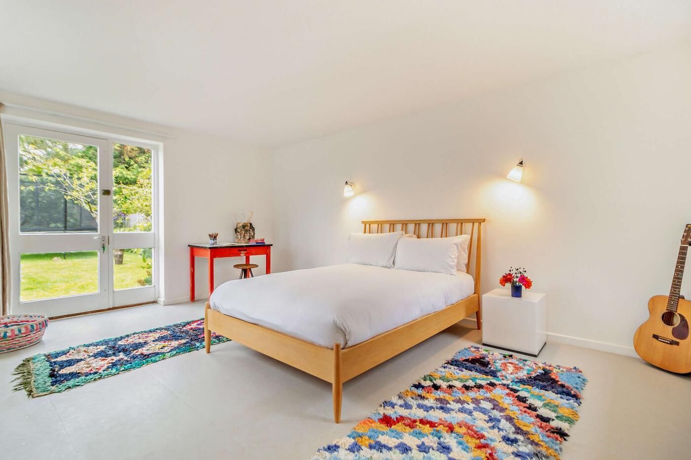 A bedroom with a wooden bed, a red desk, and a guitar.