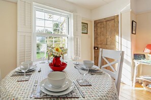 Une table à manger dressée avec de l’assiette, des bols et des couverts blancs, un vase rouge contenant des fleurs, et une porte en bois en arrière-plan.