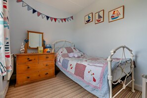 Une chambre avec un lit simple, une commode en bois et un miroir.