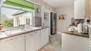 Een moderne keuken met een roestvrijstalen koelkast, witte kastjes, een raam met een groene gordijntje, en een betegelde spatwand.