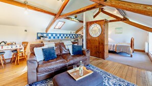 A cozy loft-style living space with a wooden ceiling, a dining area with a table and chairs, a kitchenette, and a bedroom with a bed.