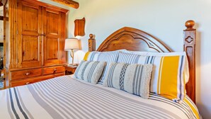 A bedroom with a large wooden bed, a nightstand, a wooden wardrobe, and a lamp.