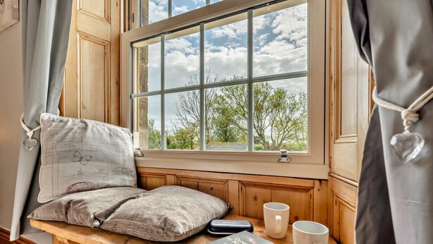 Ein gemütliches Zimmer mit einer hölzernen Bank, einem Fenster mit Blick auf Bäume, einem Buch und zwei Tassen.