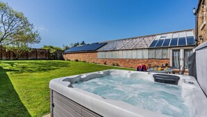 Ein Whirlpool im Garten mit einem Haus aus Ziegeln, einem Solardach und einem Rasen.
